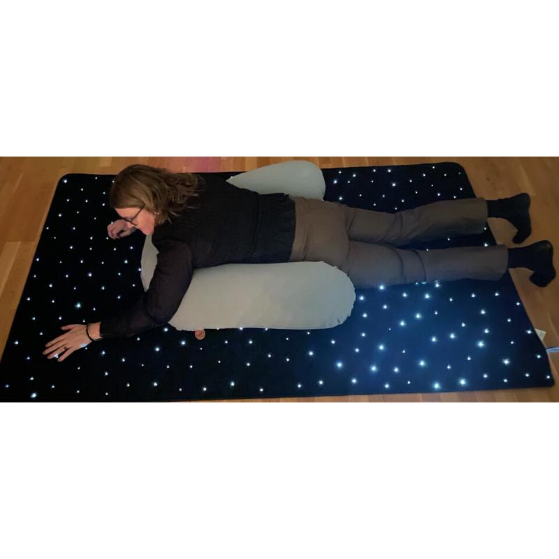 Person lying on a pillow on the TFH Fiber Optic Starfield Carpet