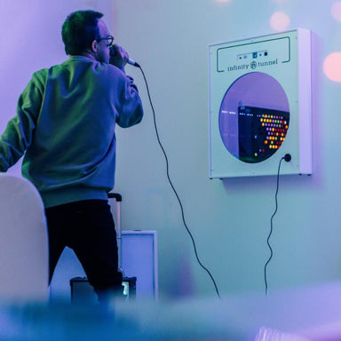 Person singing into a microphone in front of a colorful TFH Infinity Tunnel