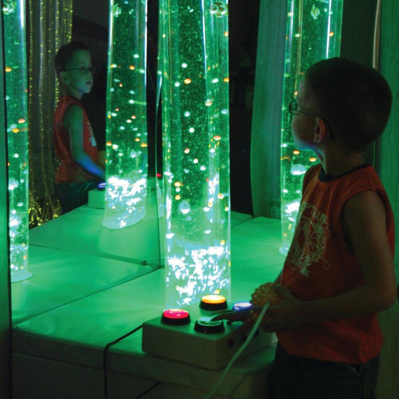 child interacting with TFH Interactive Bubble Tubes in sensory room with green lighting