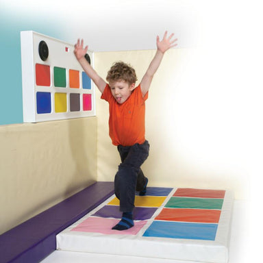 Child playing on colorful TFH Musical Squares with a wall of color swatches in a sensory room.