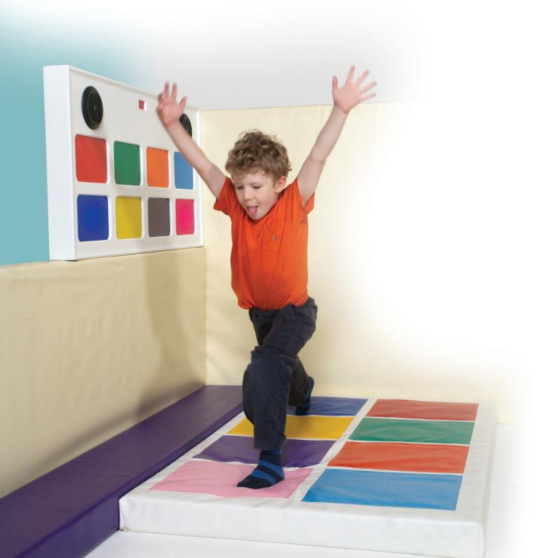 Child playing on colorful TFH Musical Squares with a wall of color swatches in a sensory room.