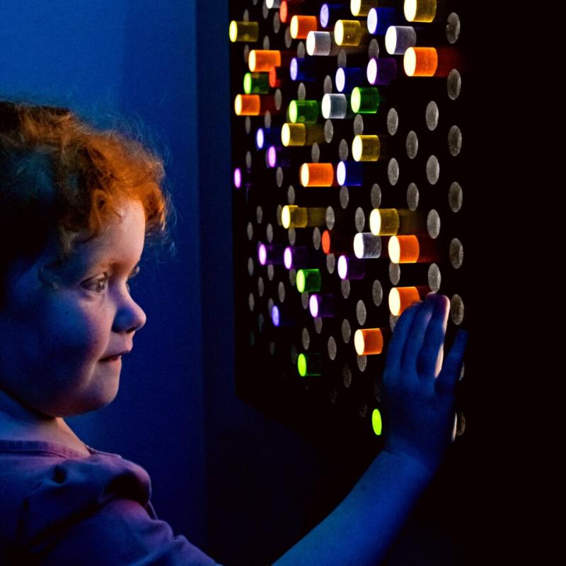 Child interacting with the TFH Rod Wall Light Panel with dark background