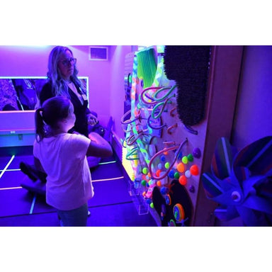 Two people in a room with UV lighting, interacting with a colorful TFH UV Textured Wall